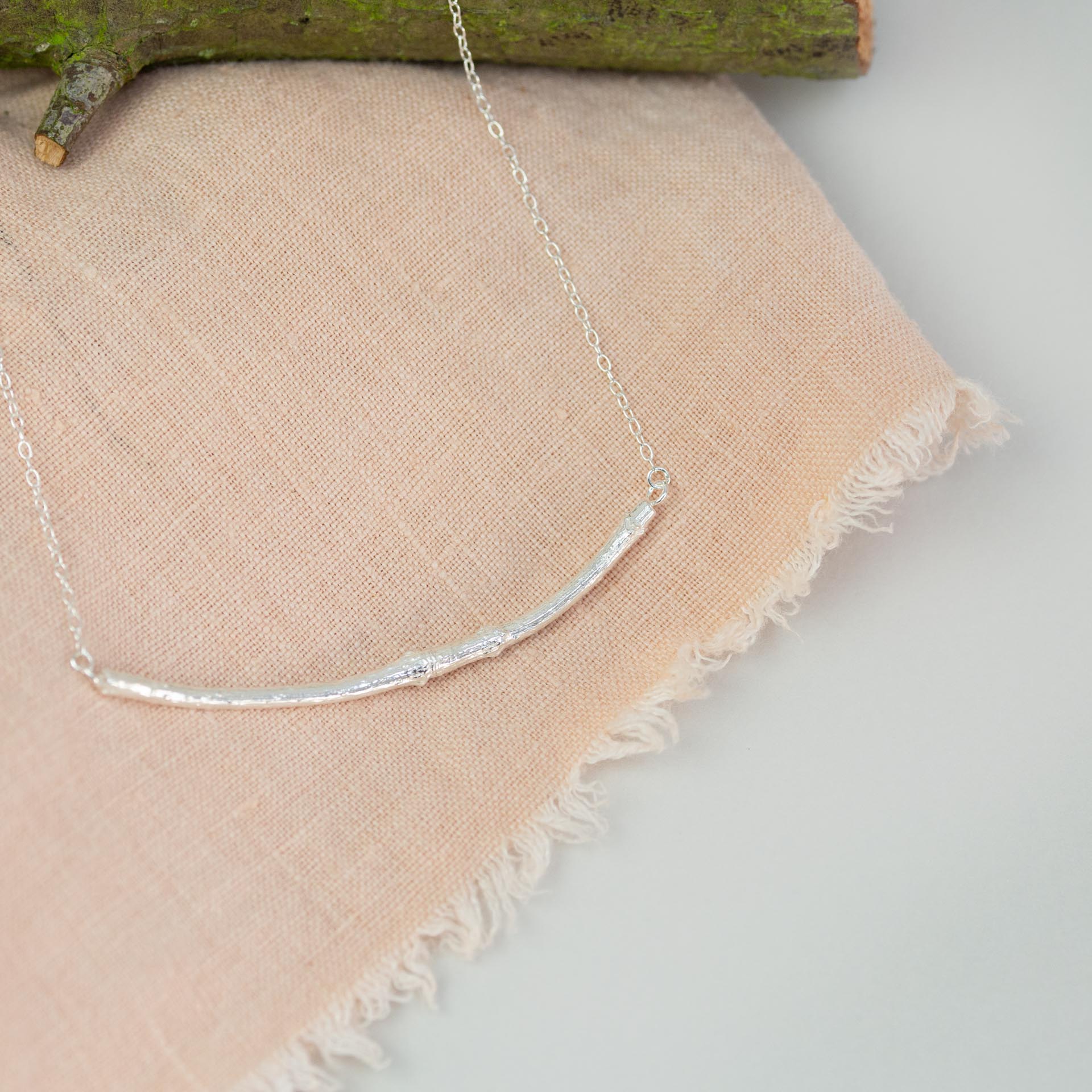 silver smooth twig necklace on pink cloth near wooden branch