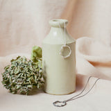 silver Wreath Pendant and oxidised wreath pendant resting near vase with dried flora