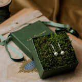 Pair of pearl earrings in a green box with moss on a patterned surface