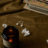Pearl earrings and a candle on a brown fabric surface