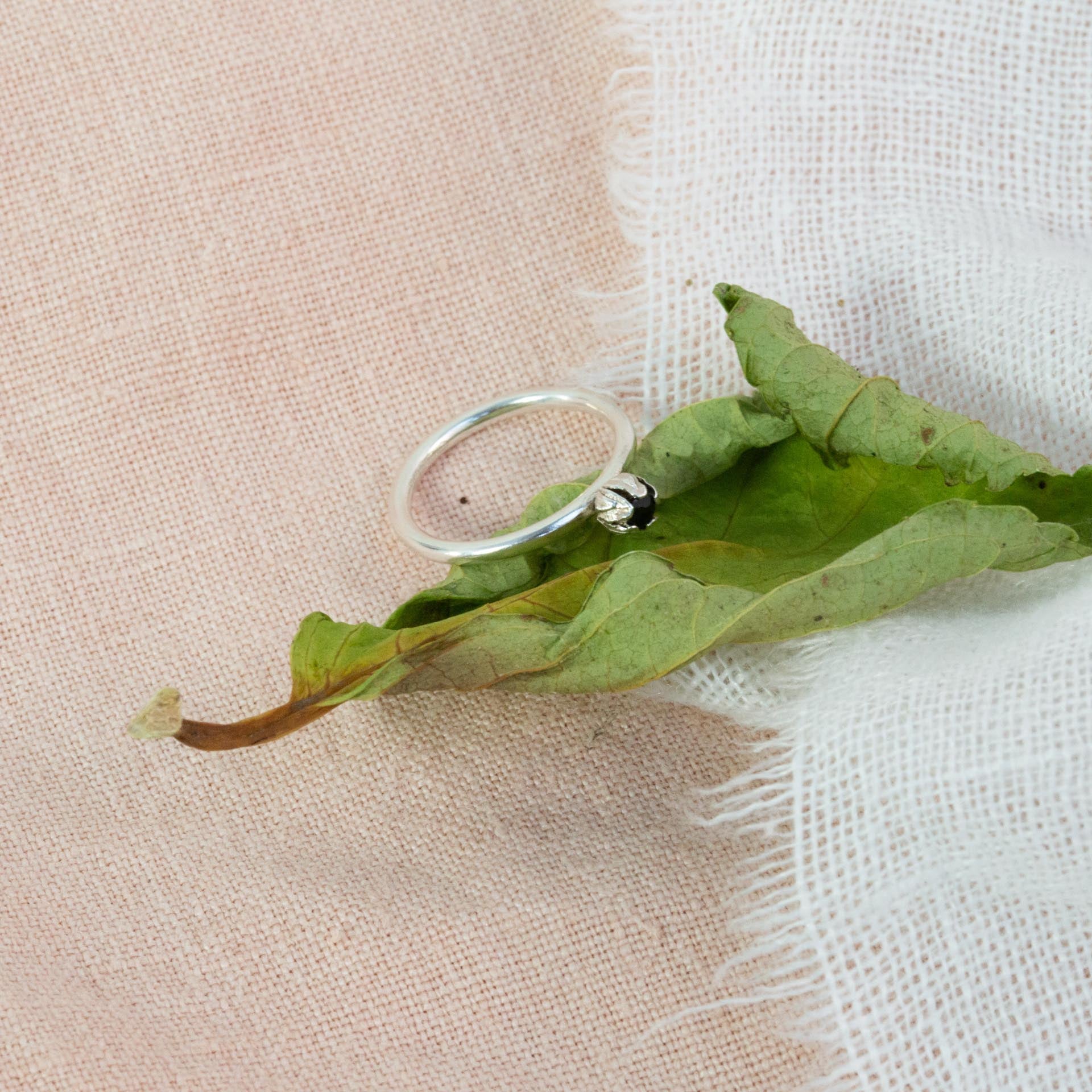 Silver engagement ring rested on green leave above pink and white cloth 
