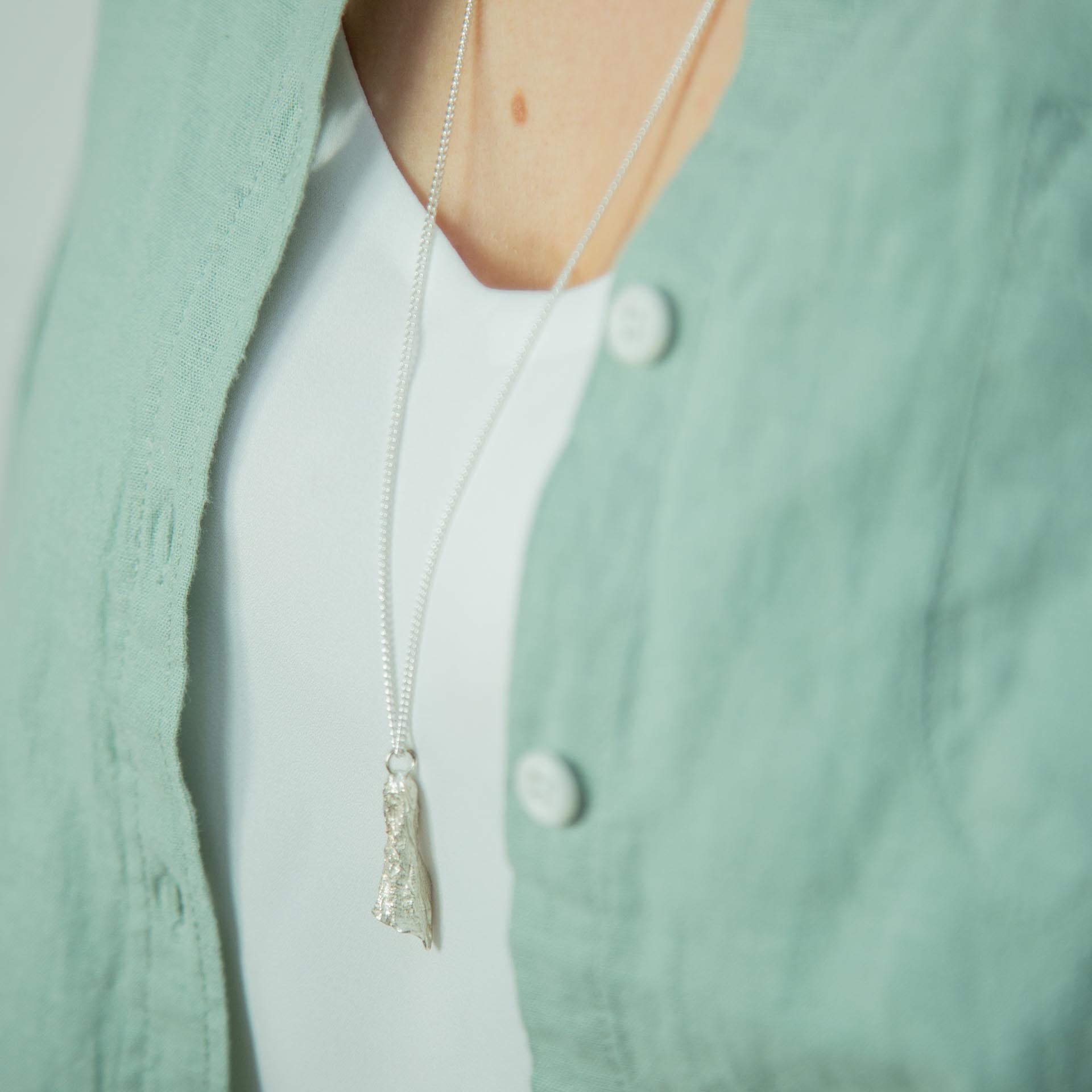silver foxglove pendant necklace on model hanging above a green shirt and white t-shirt 
