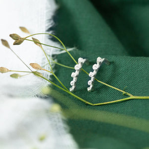 Silver Ivy bud half hoop earrings resting on green and white cloth with dried flowers in the foreground