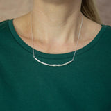 silver smooth twig necklace modelled around neck resting on green t-shirt