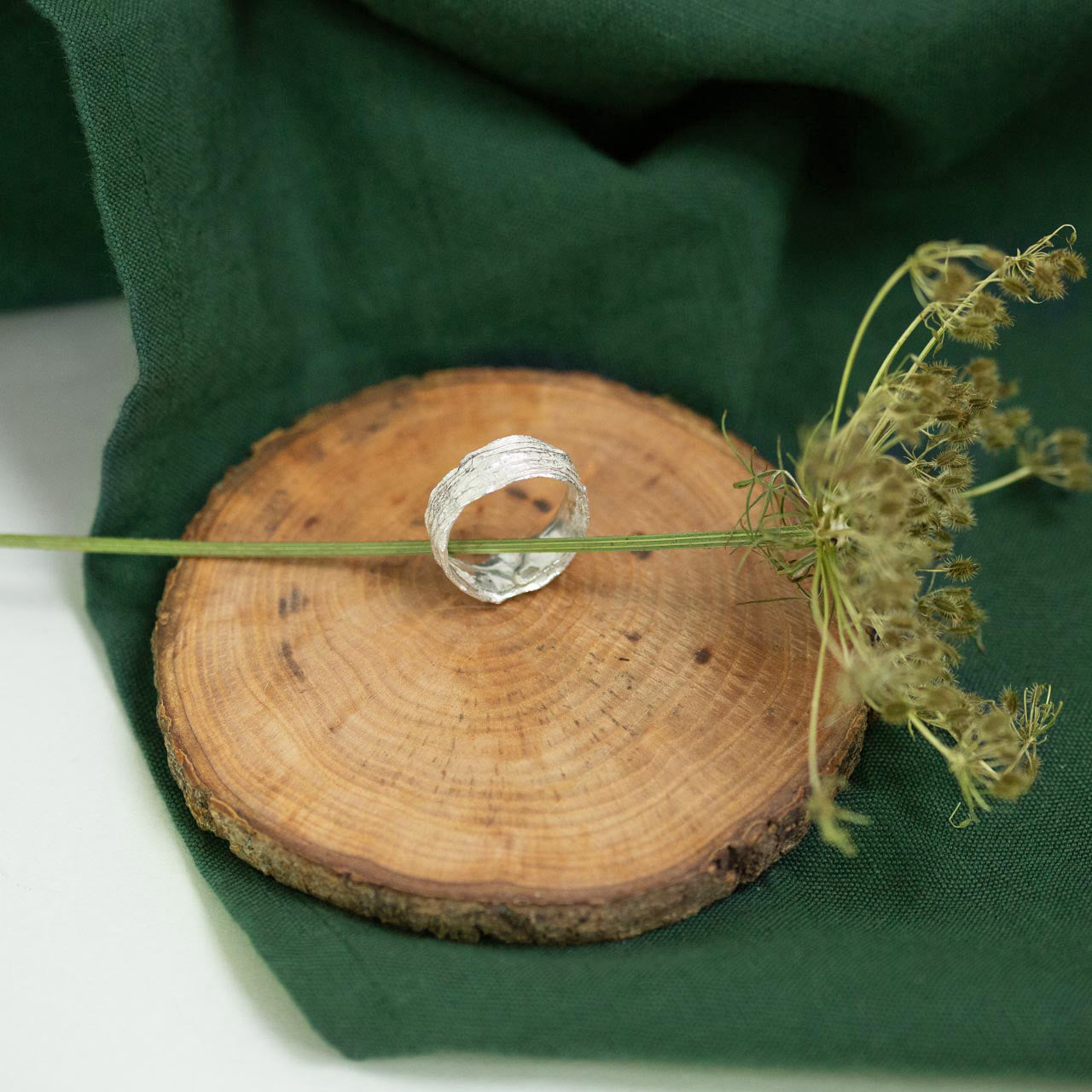 silver Snow Drop Leaf Wrap Ring on wood next to green cloth and dried flora