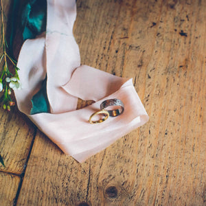 gold and silver wedding rings resting on pink cloth above wooden boards