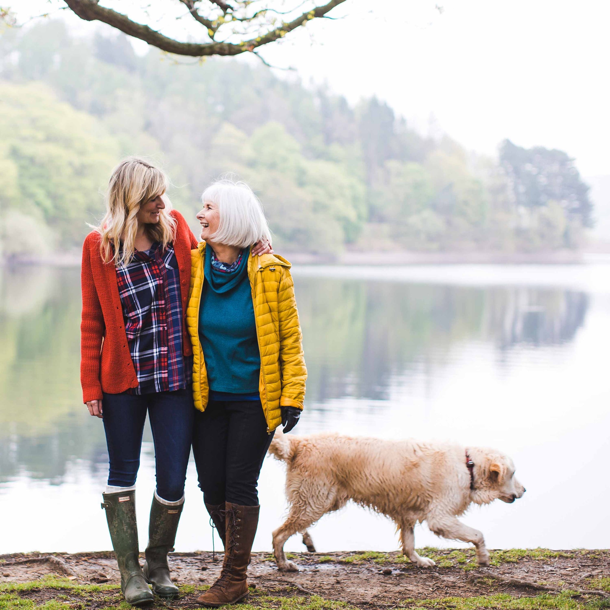 mum and daughter laughing near lake next to dog