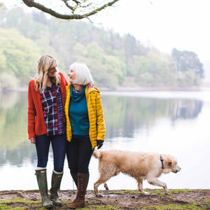 mother and daughter laughing near lake with dog 