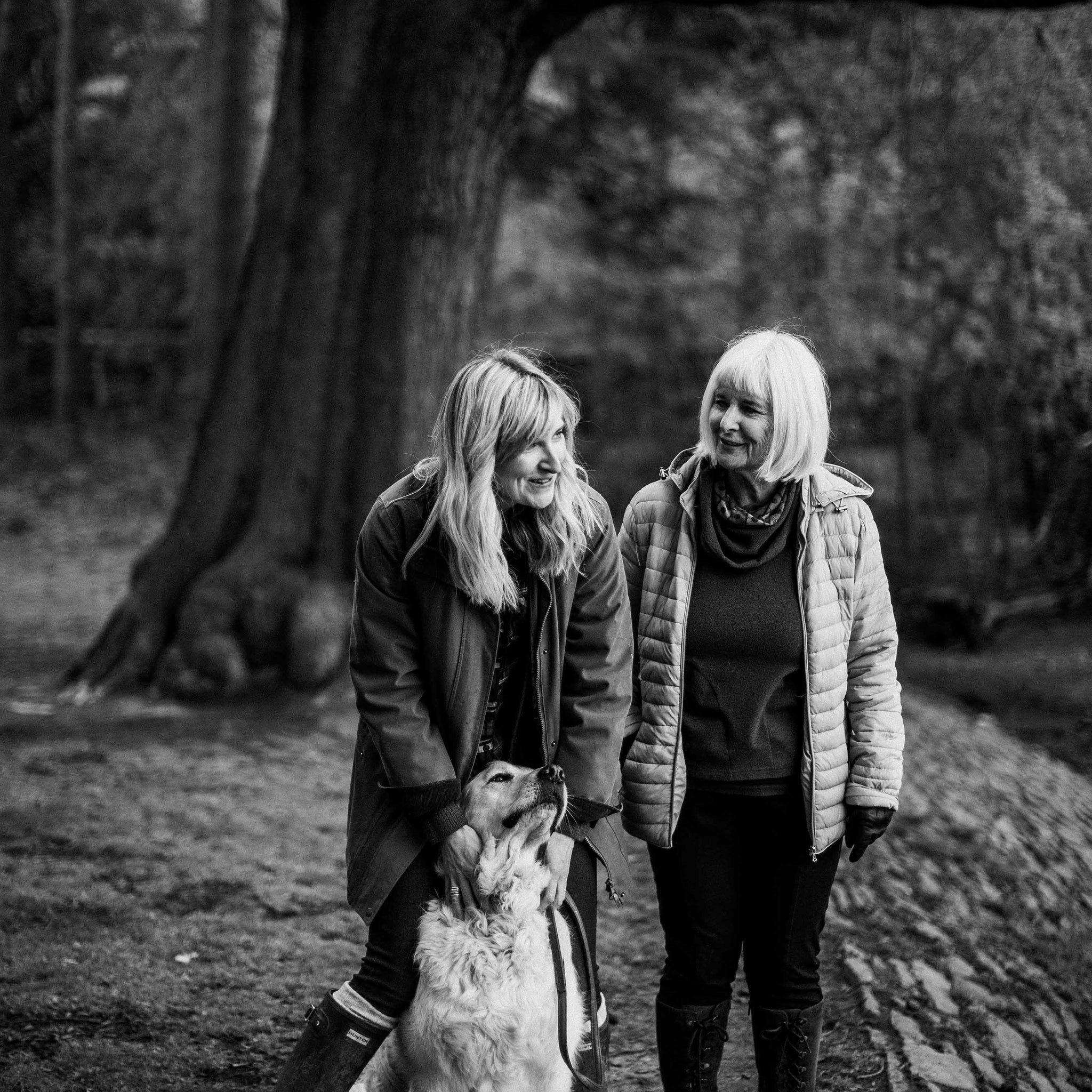 black and white of mum and daughter walking in forest with dog