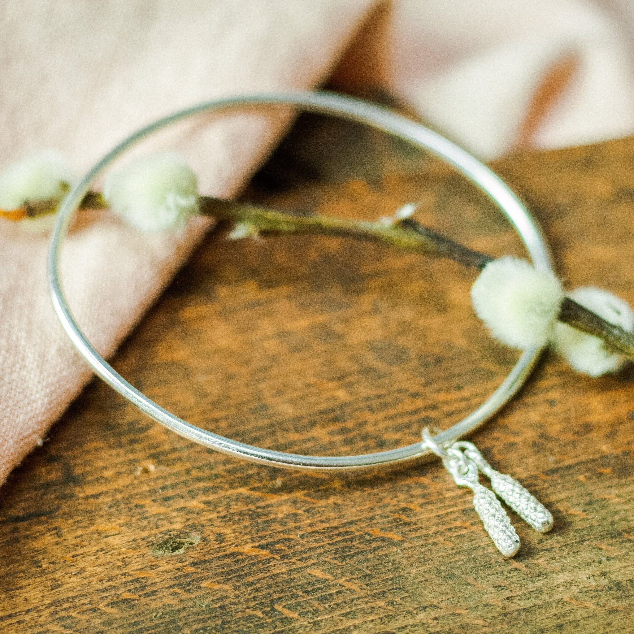 silver catkin bangle on pink cloth and wood
