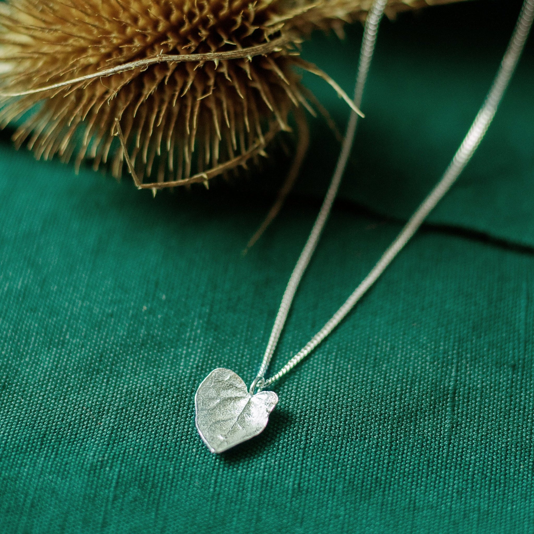 silver ivy leaf necklace on green background with dried flower