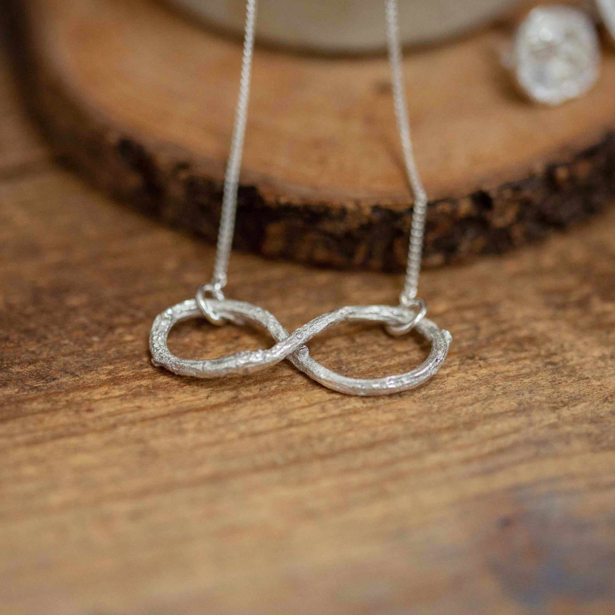 Infinity shape necklace resting on wooden background 